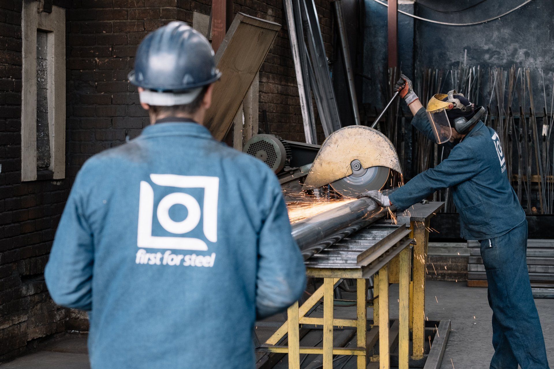 Two NJR Steel staff members are working in a factory and one is wearing a first-for-steel jacket