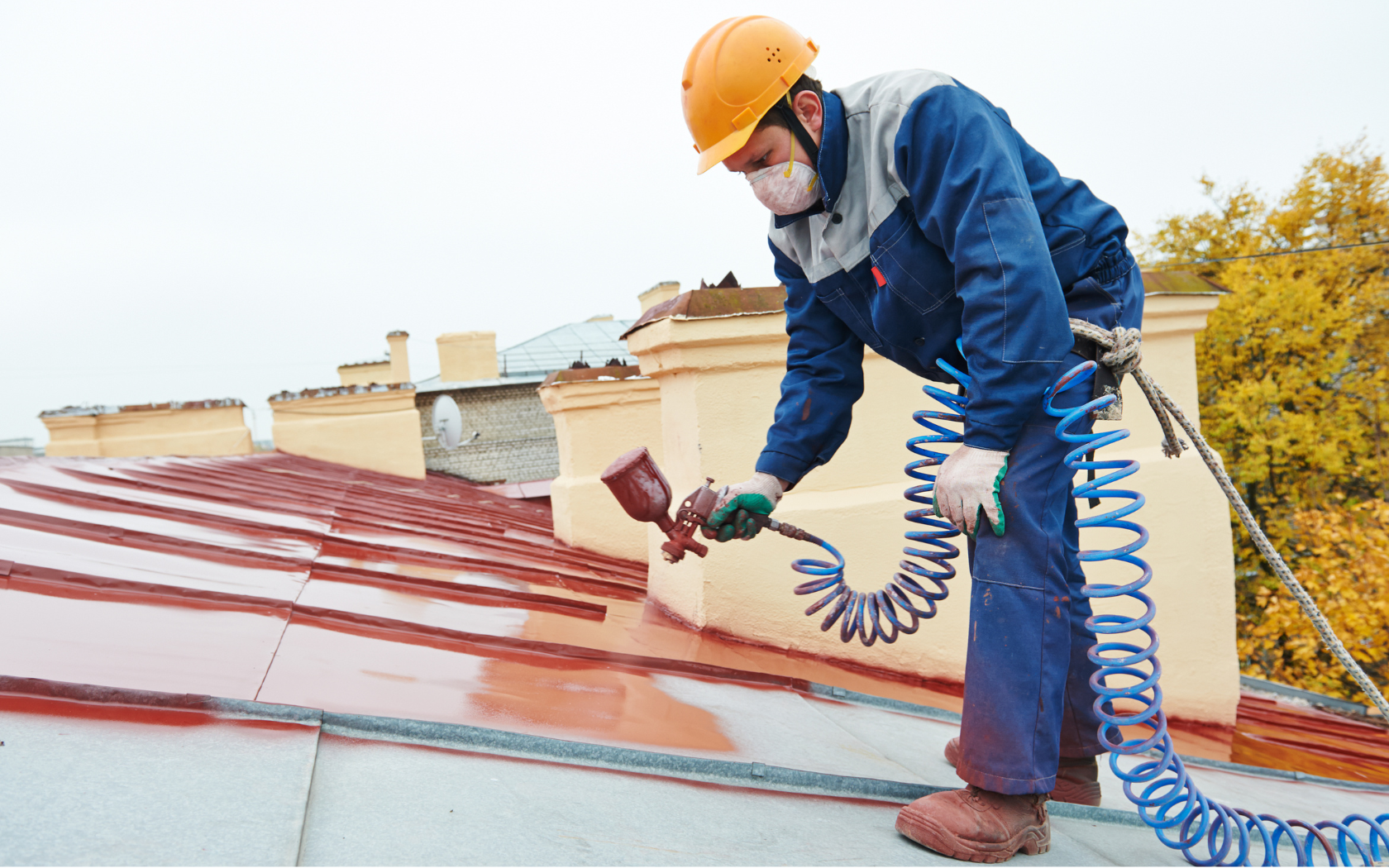 A man wearing a helmet and mask is spraying paint on a roof.