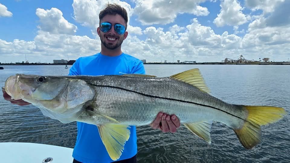 A man in a hat is holding a large fish in his hands.