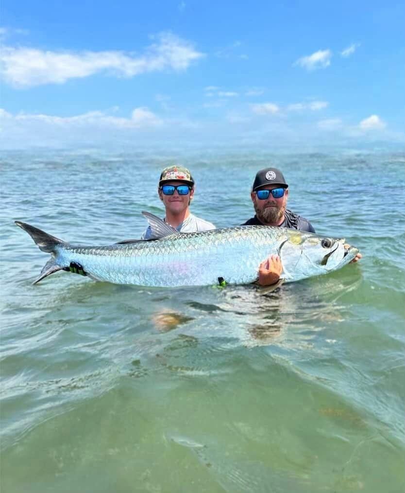 Two men are holding a large fish in the water.