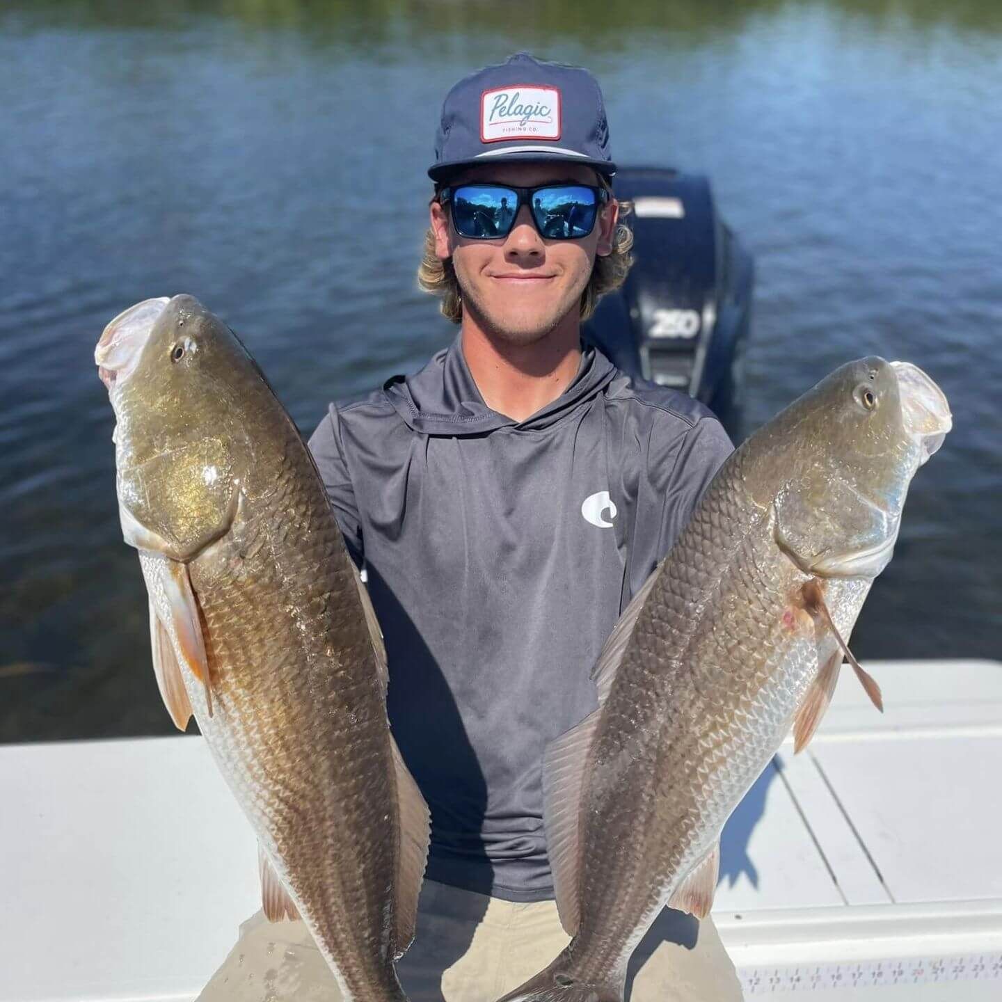 A man wearing sunglasses and a hat is holding two fish