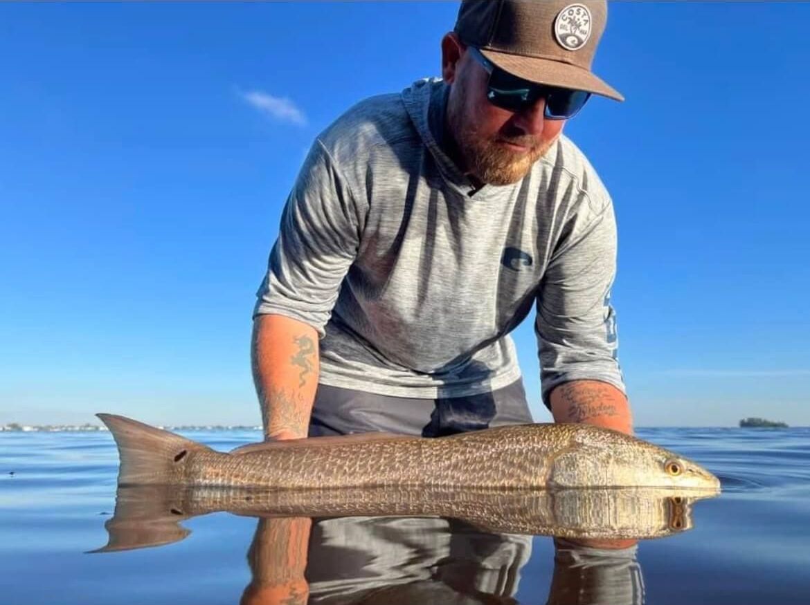 A man is holding a large fish on the beach.