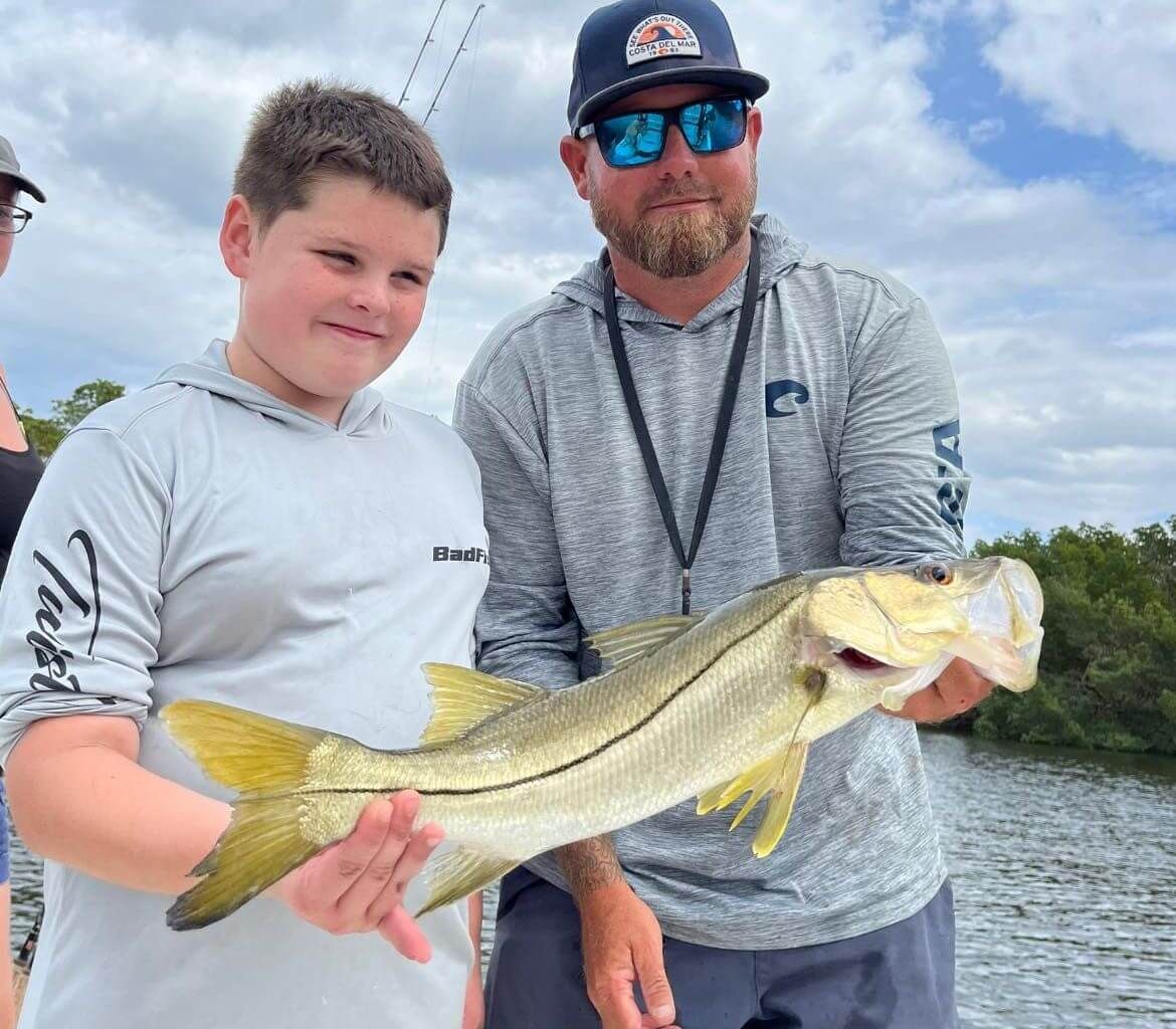 A man and a boy are holding a large fish in their hands.