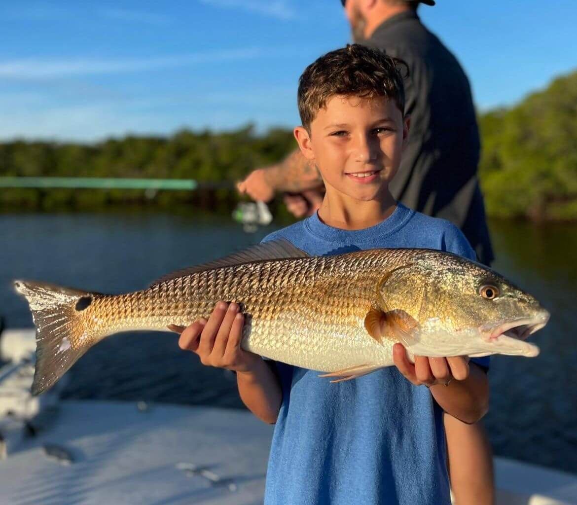 A young boy is holding a large fish in his hands