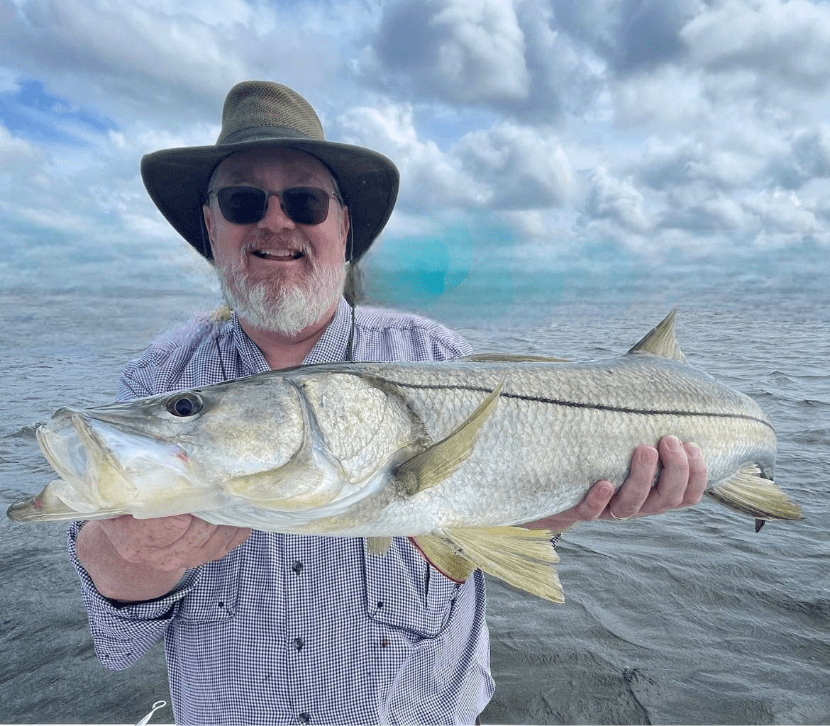 A man in a hat is holding a large fish in his hands.