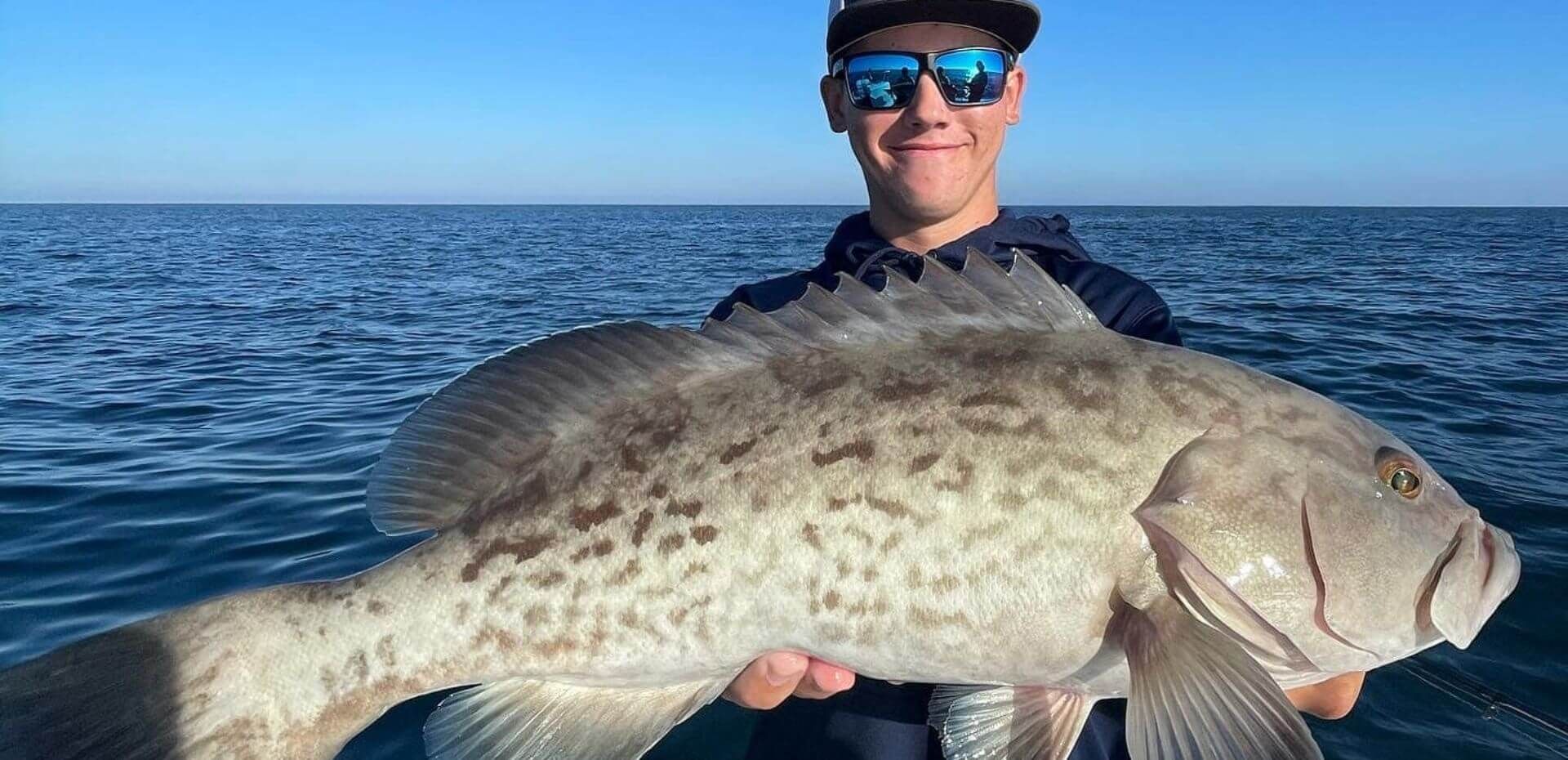 A man is holding a large fish in his hands in the ocean.