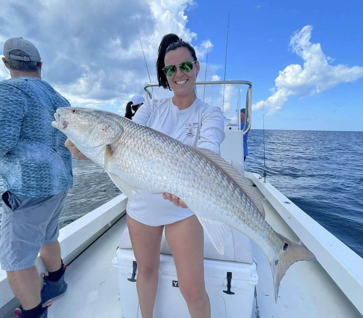 A woman is holding a large fish on a boat.