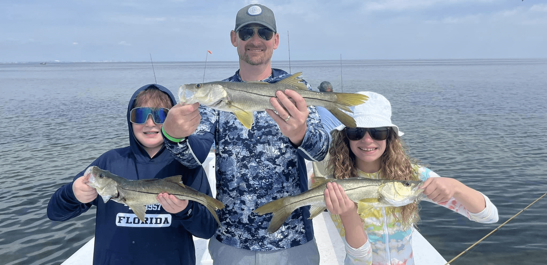 A man and two children are holding fish on a boat.