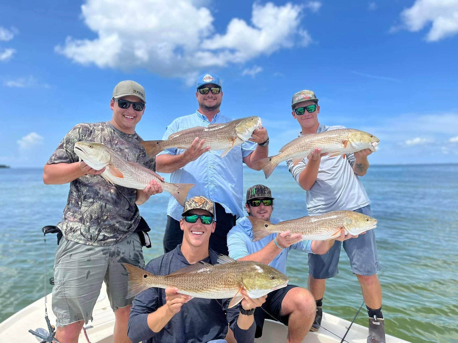 A group of men are standing on a boat holding Redfish.