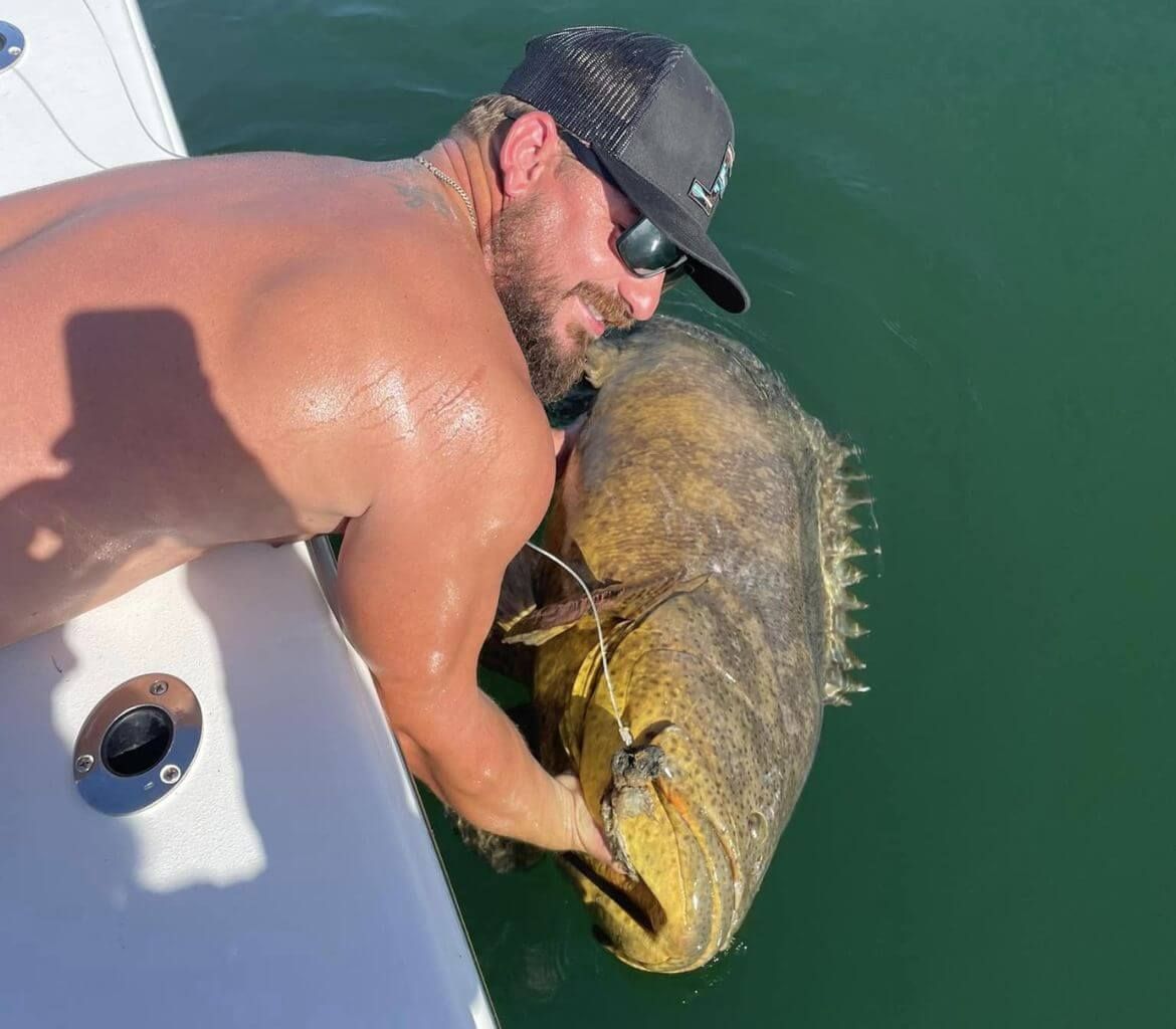 A shirtless man is holding a large fish on a boat