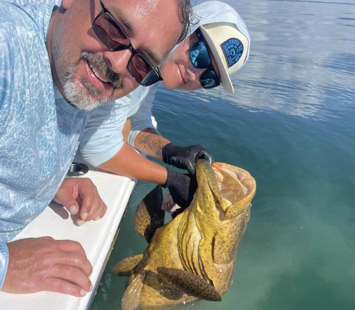 Two men are holding a large fish in the water.