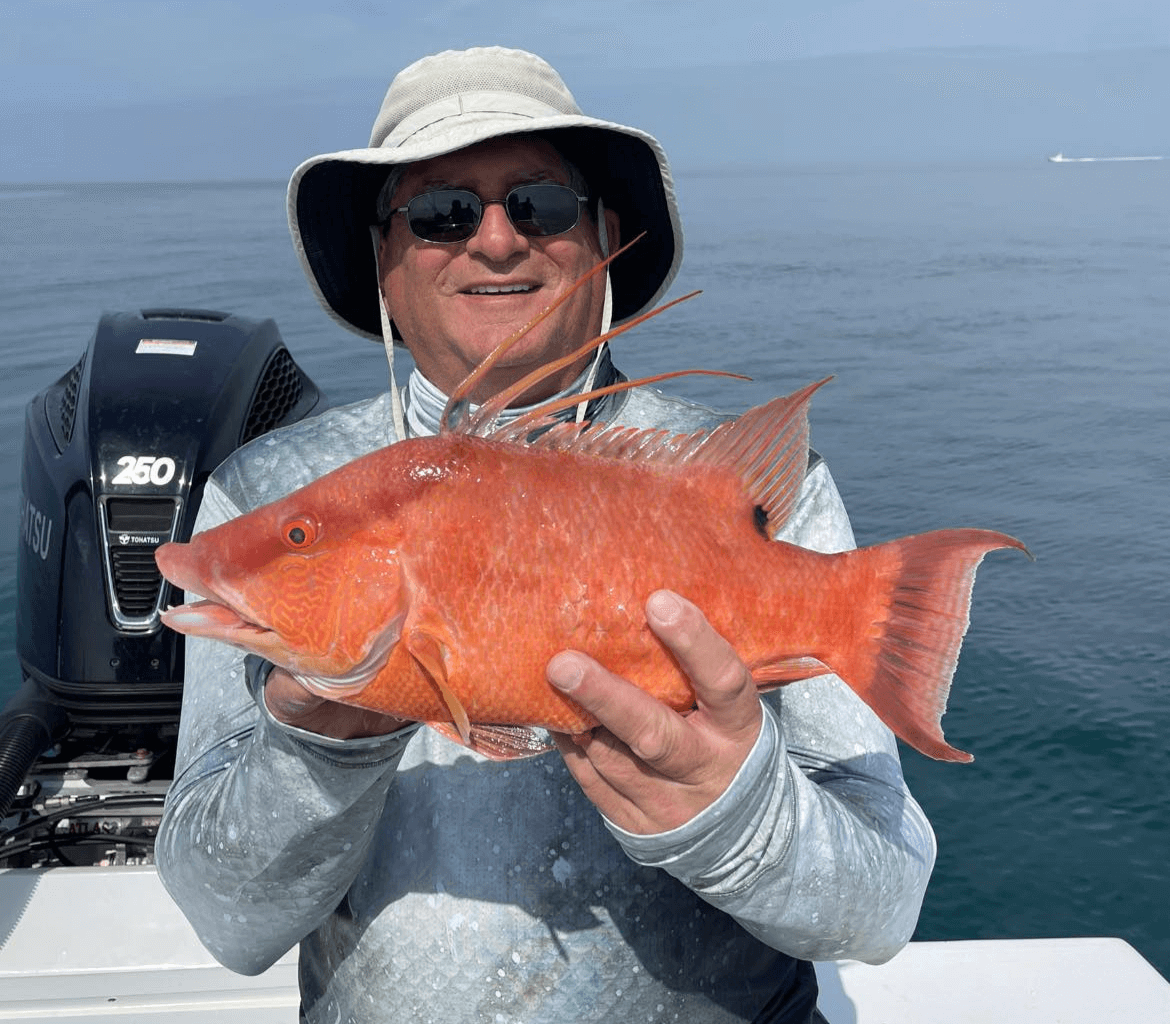 A man is holding a red fish in front of a mercury motor