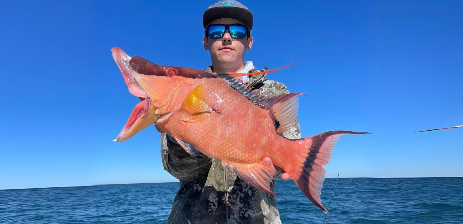 A man is holding a large red fish in the ocean.