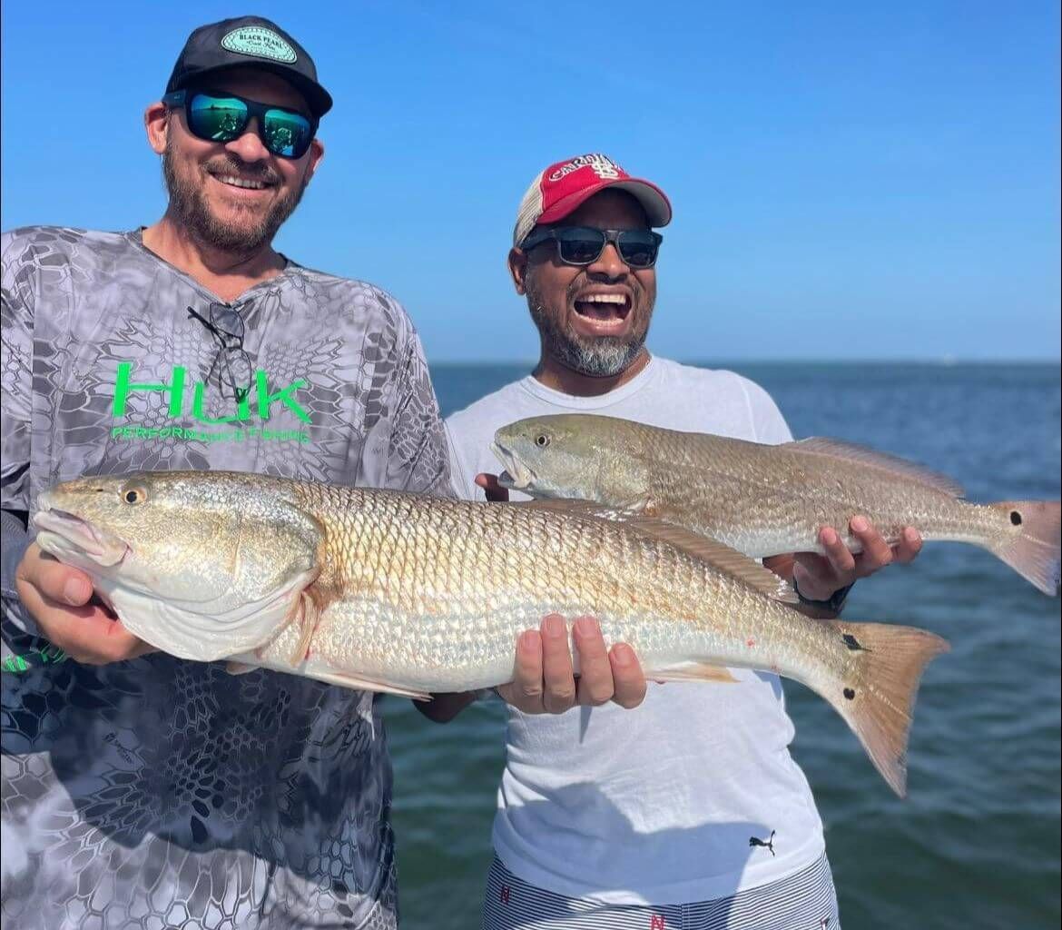 Two men are holding large fish in their hands in the water