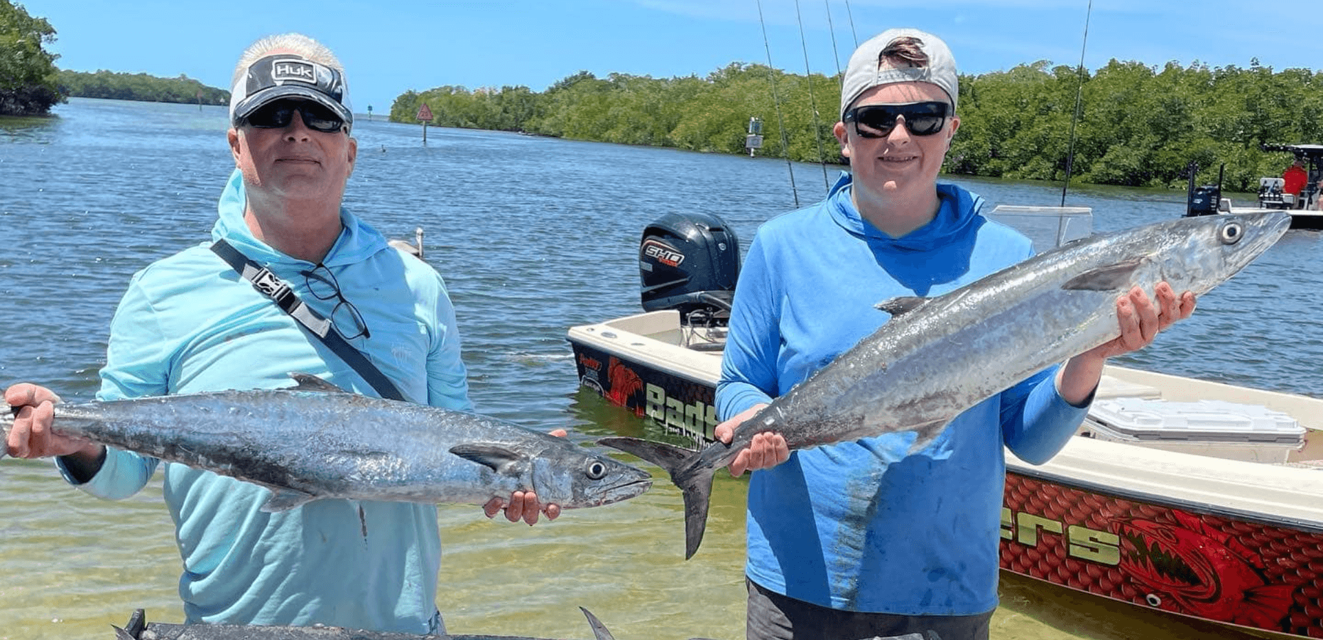 Two men are holding fish in front of a boat in the water.