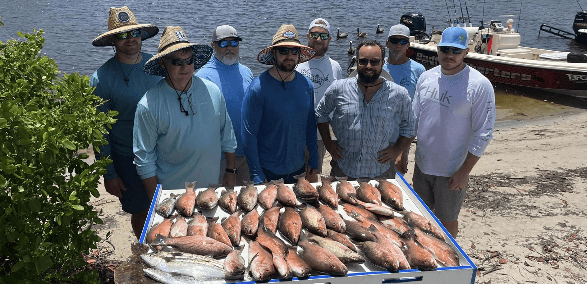 A group of men are standing around a tray of fish on the beach.