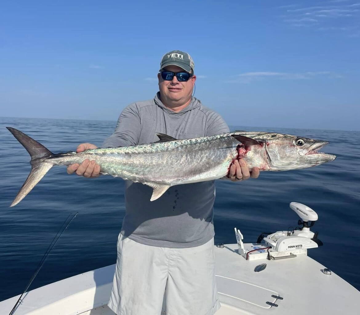 A man is holding a large fish on a boat in the ocean.