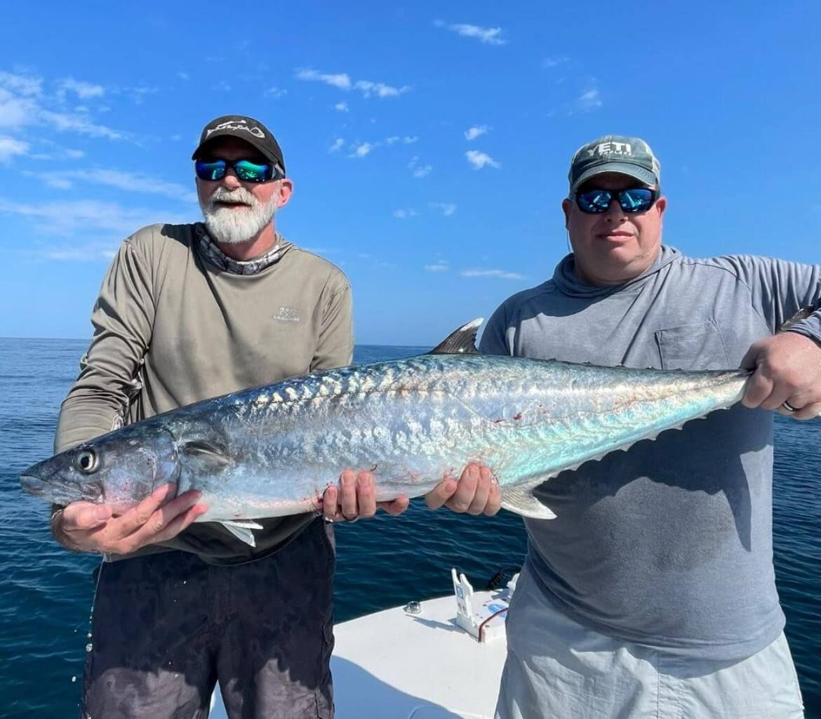 Two men are holding a large fish on a boat