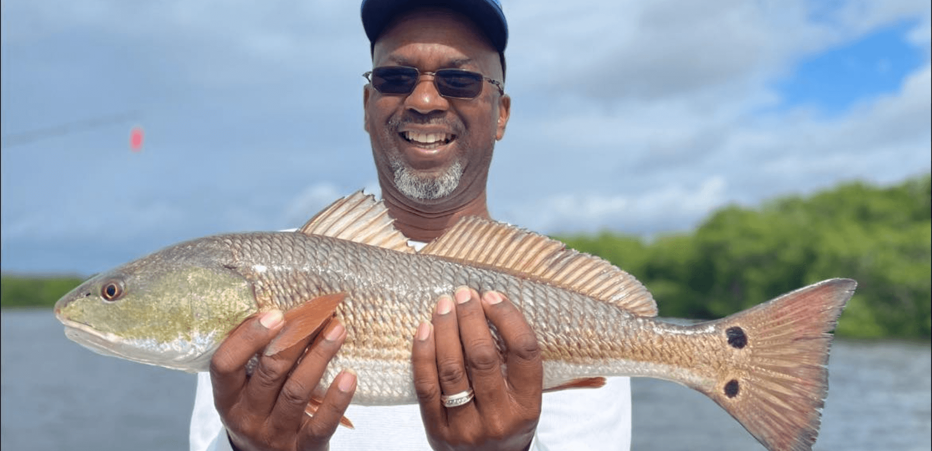 A man is holding a large redfish in his hands.