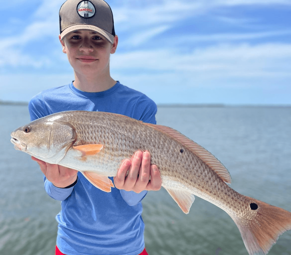 A young man is holding a large red fish in his hands.