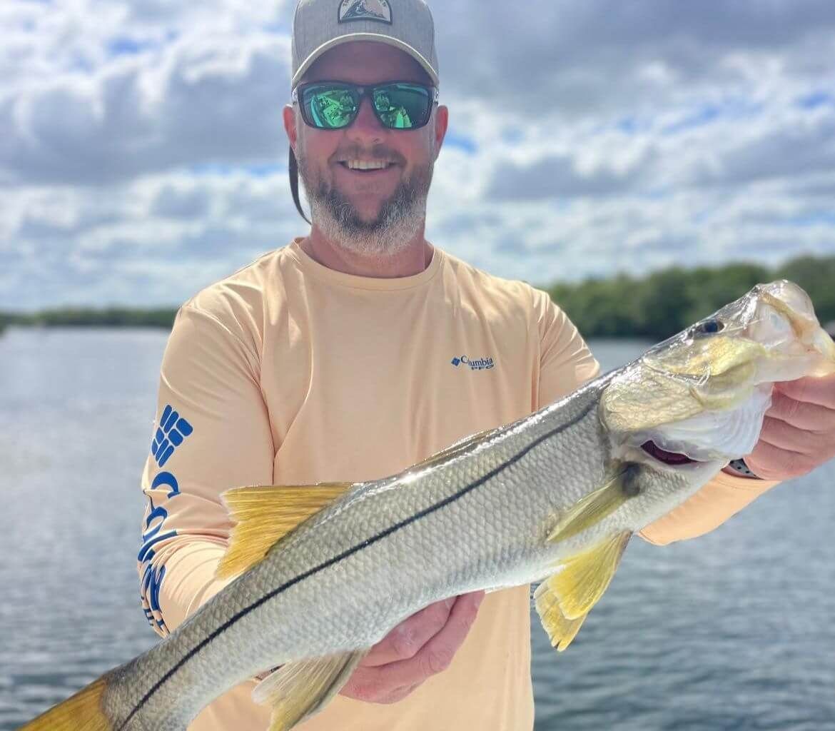 A man wearing sunglasses and a hat is holding a large fish