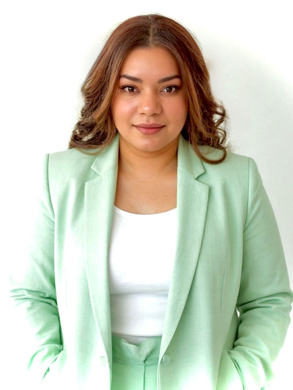 A woman is sitting at a desk with a laptop and a vase of flowers.