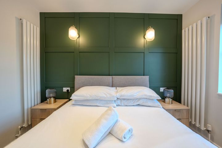 A bedroom with a bed , nightstands , and a green wall.