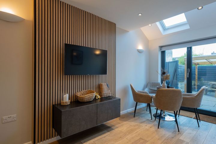 A living room with a table and chairs and a flat screen tv on the wall.