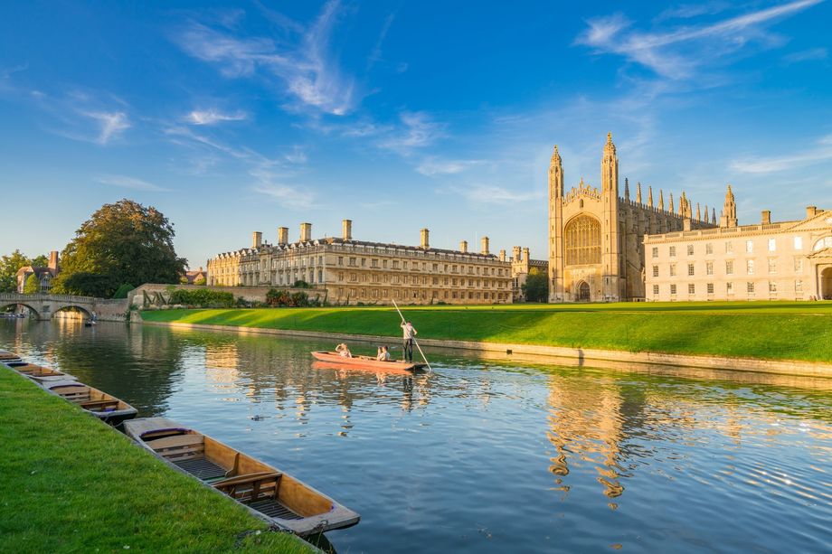 A man is rowing a boat on a river in front of a large building.