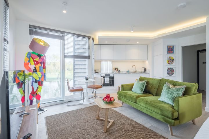 A living room with a green couch , table , chairs and a colorful statue.