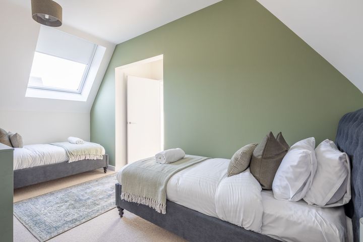 A bedroom with two beds and a green wall.
