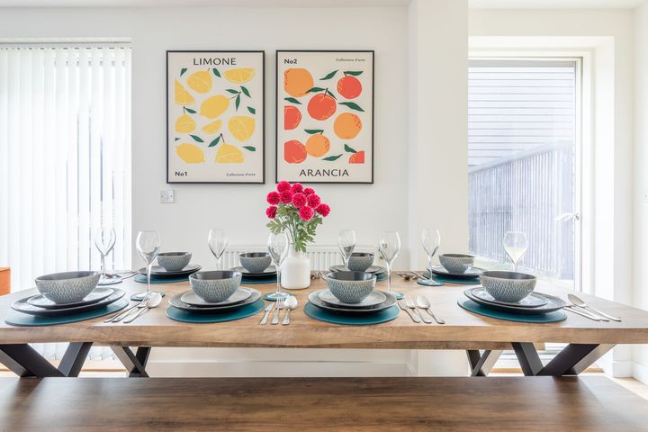 A dining room table with plates , bowls , glasses and a vase of flowers on it.