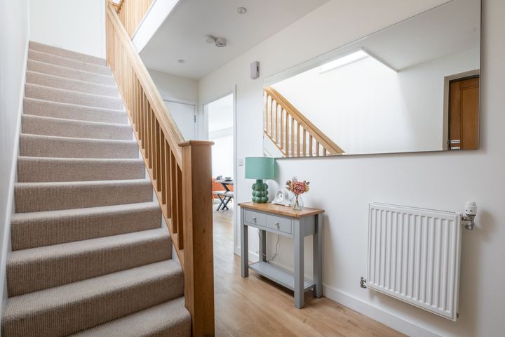 A hallway with stairs , a table and a mirror.