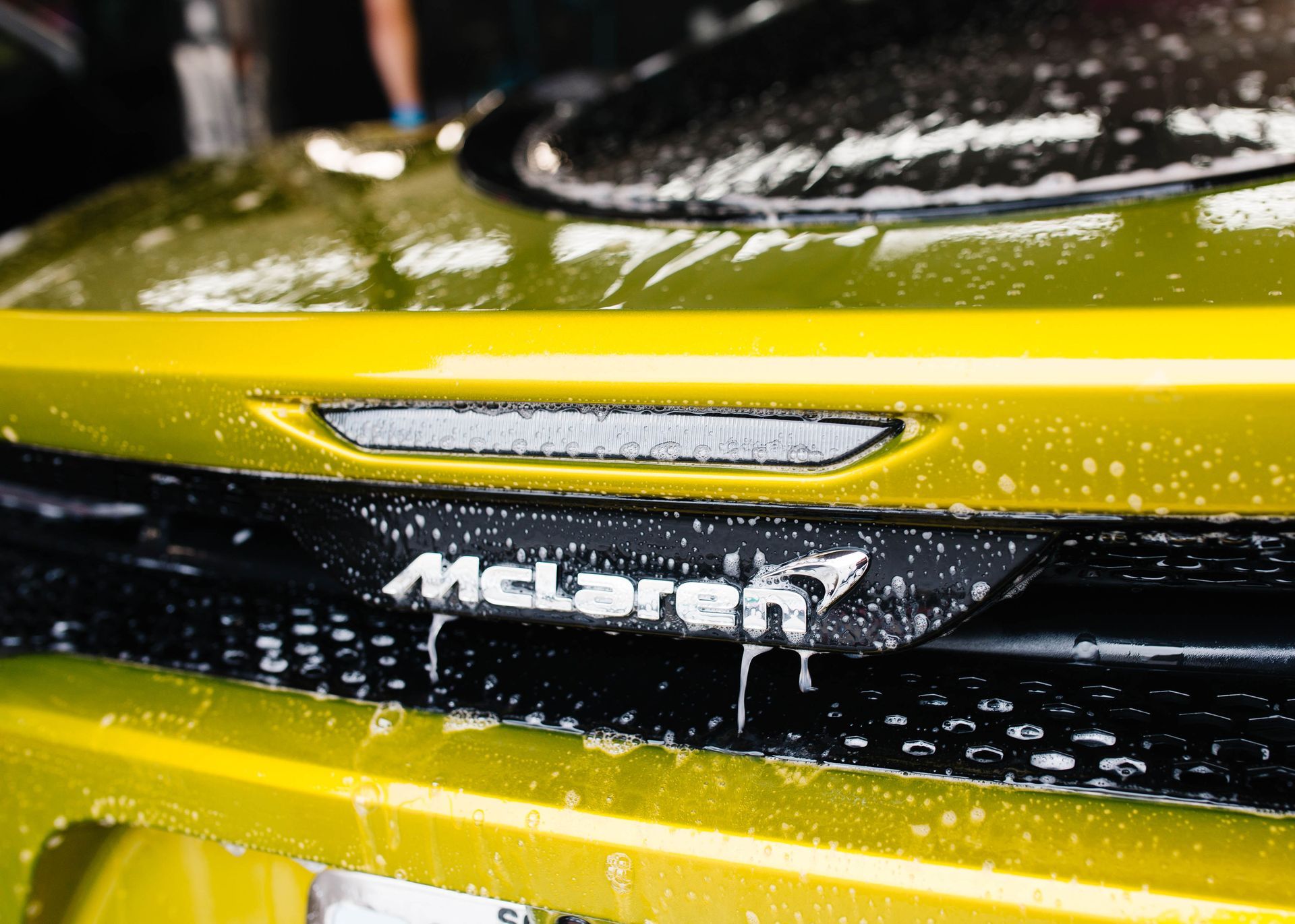 Close-up of a yellow McLaren being washed with soapy water. The car's