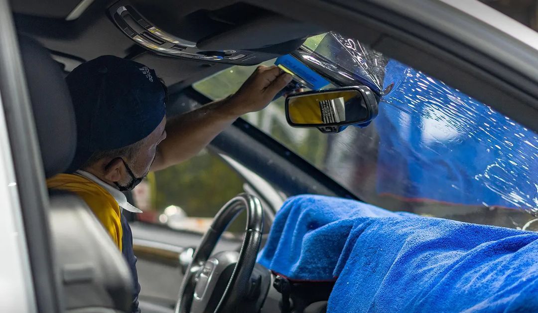 A man is cleaning the windshield of a car with a blue towel.