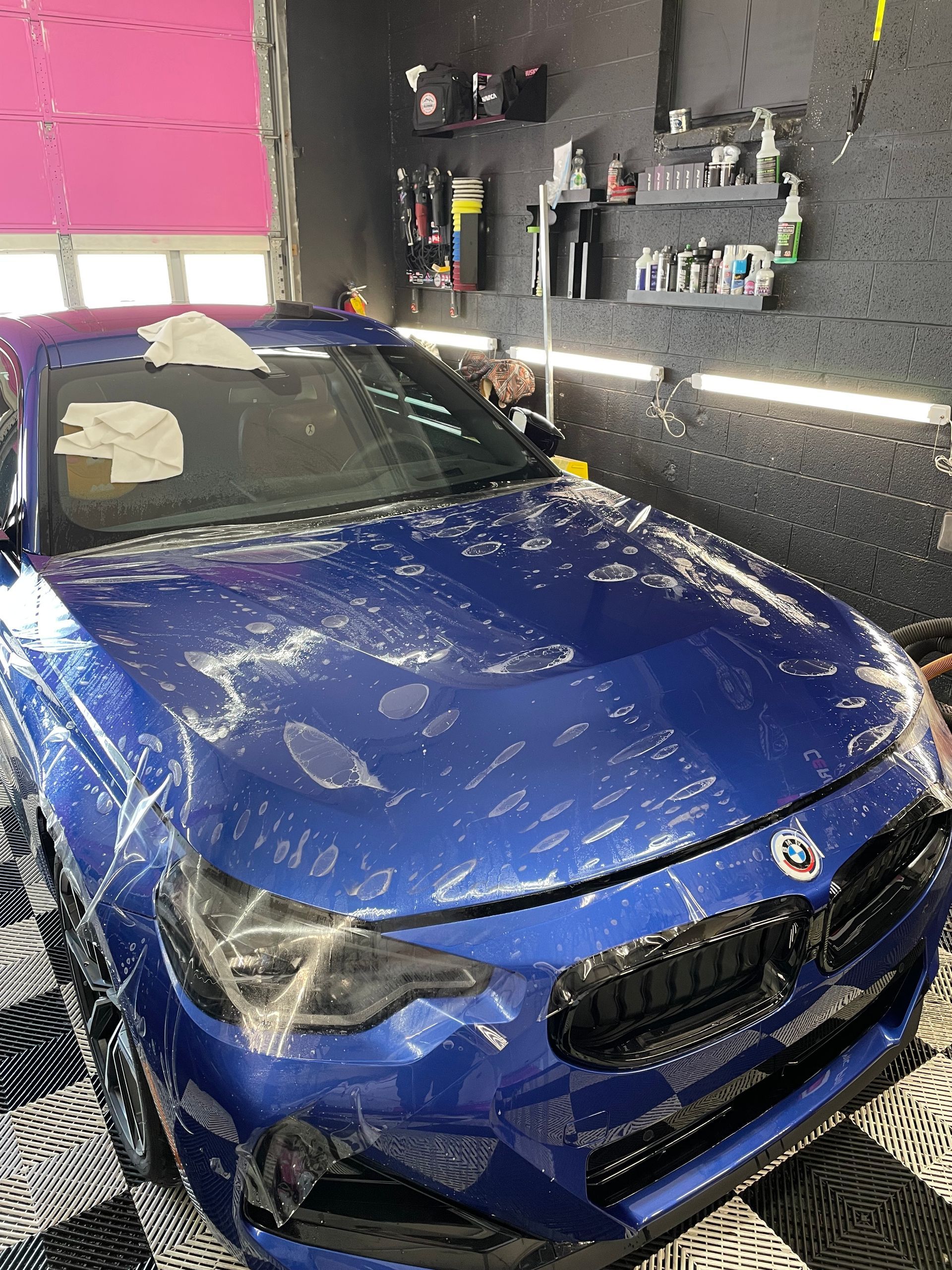 A blue car is covered in plastic in a garage.