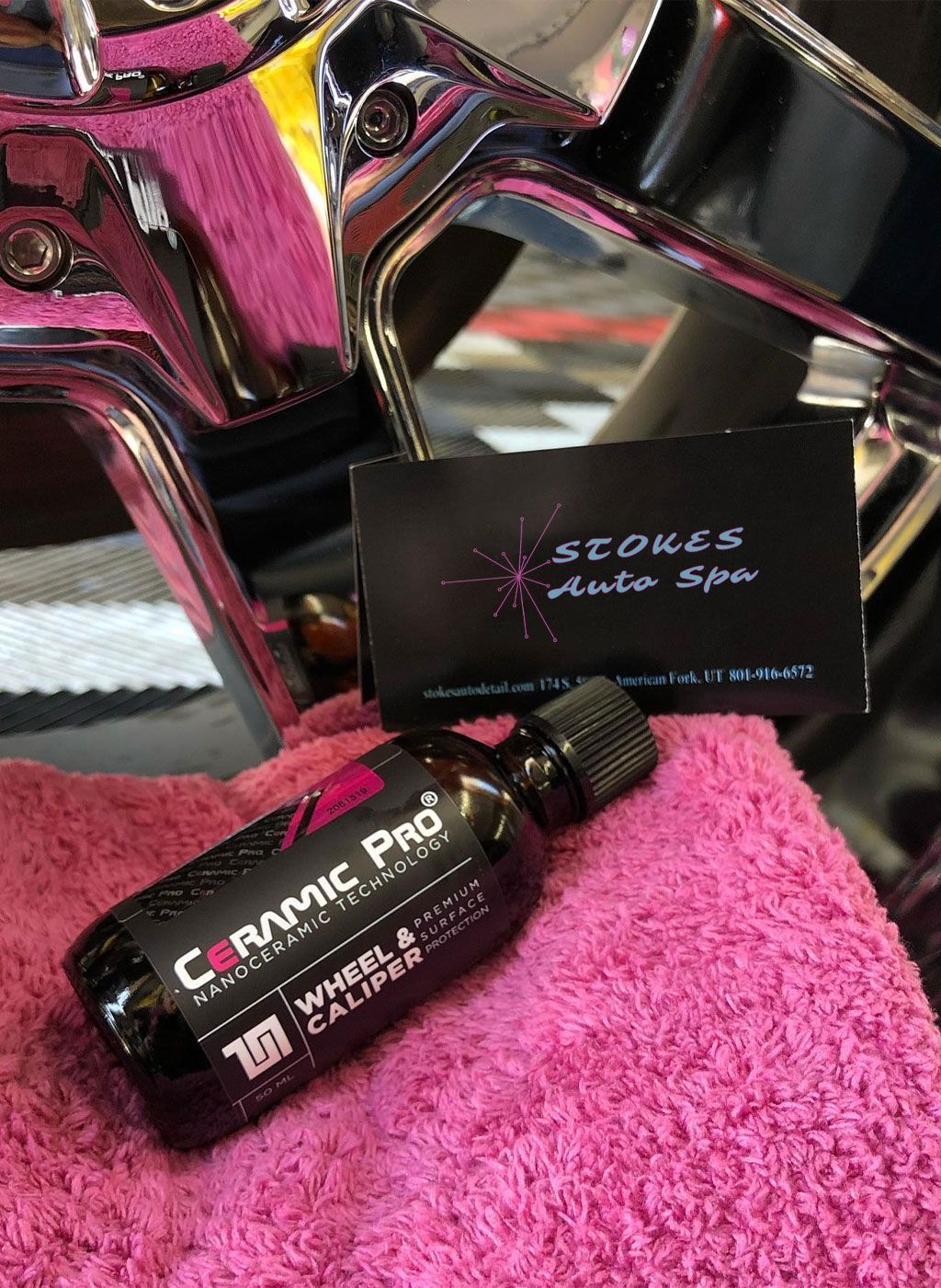 Ceramic Pro wheel & caliper coating with Stones Auto Spa business card on a pink towel near a chrome vehicle part.