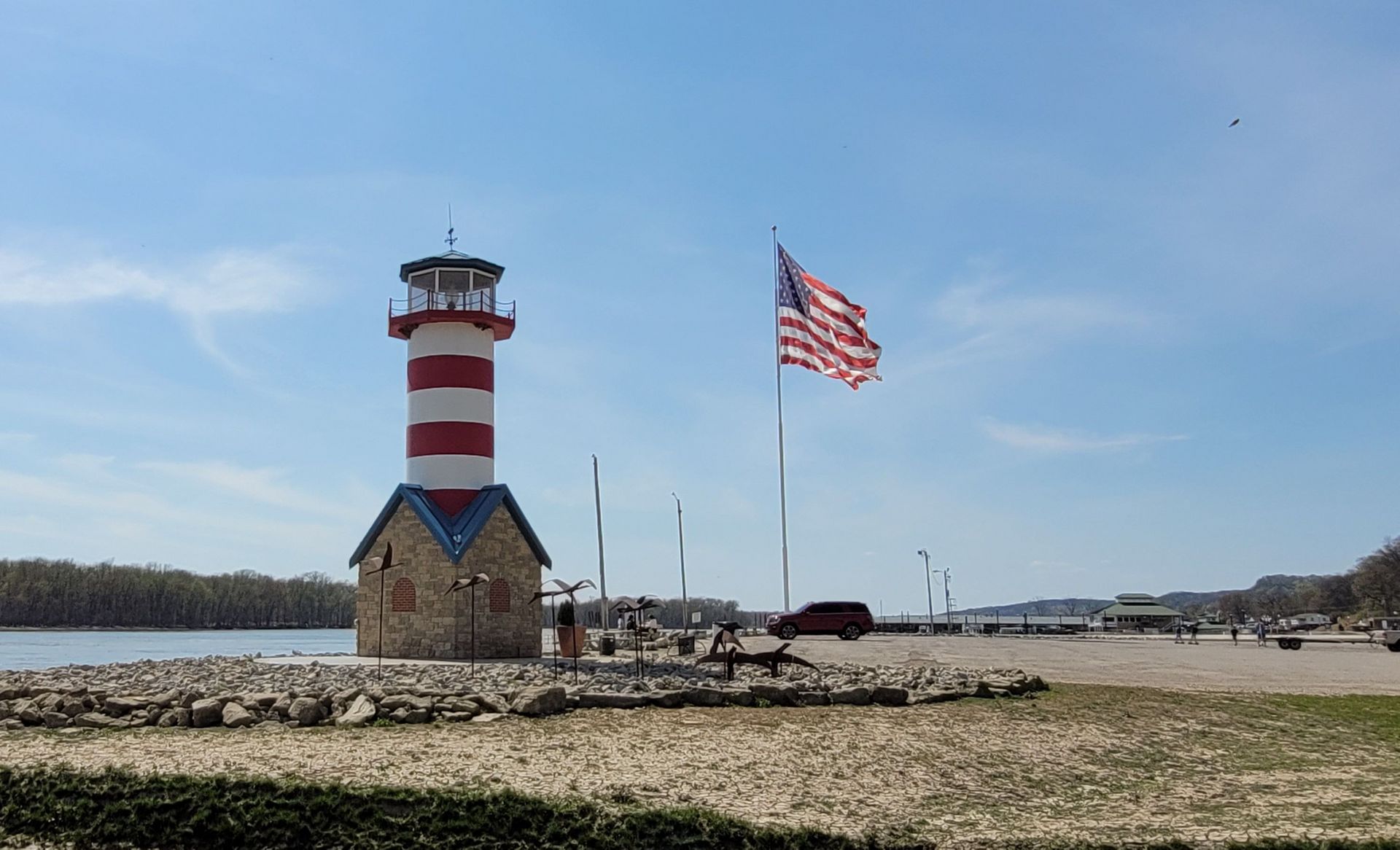 A red , white and blue lighthouse with an american flag flying in front of it.