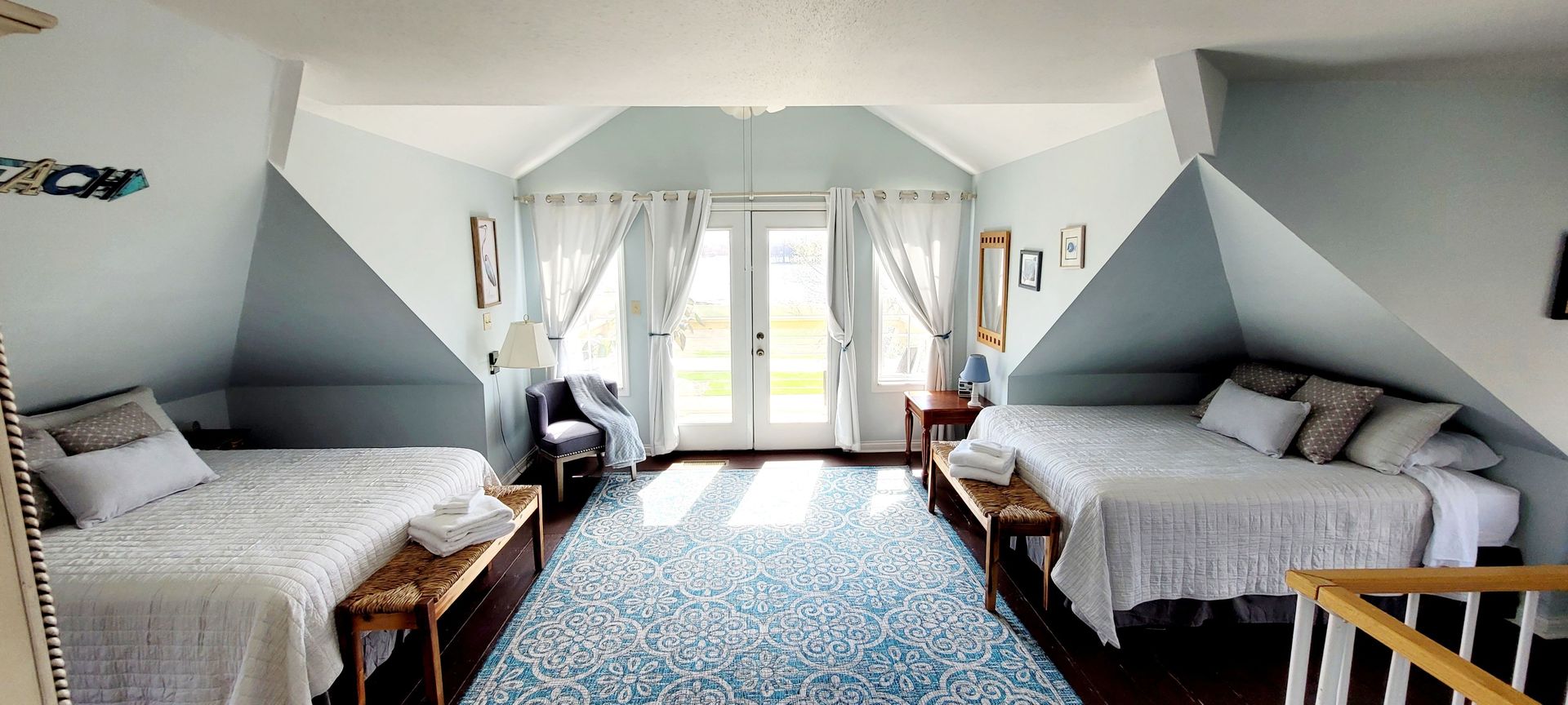 A bedroom with two beds , a bench , and a staircase.