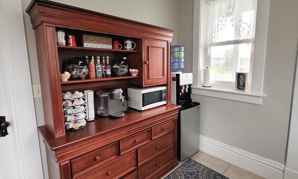 A kitchen with a hutch , microwave , coffee maker , and water cooler.