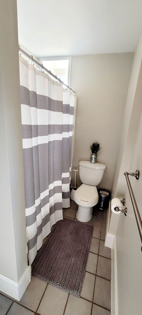 A bathroom with a toilet , shower curtain and rug.