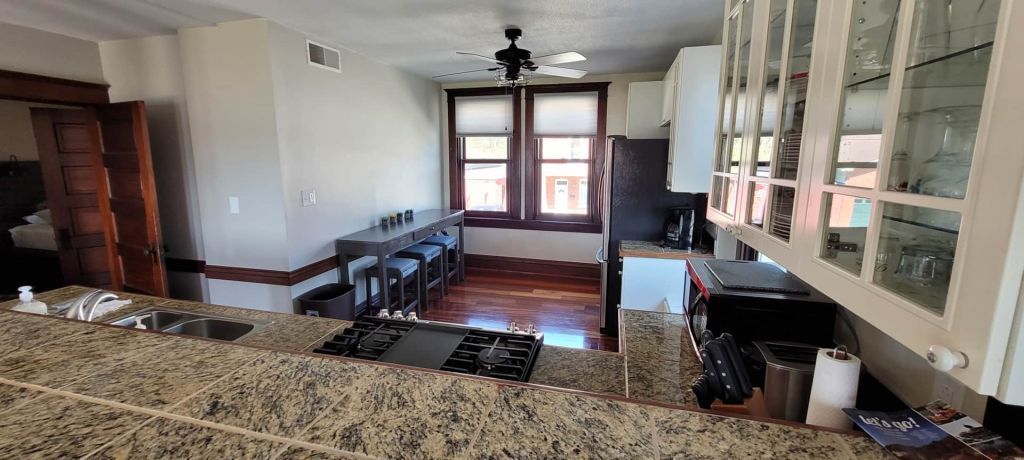 A kitchen with granite counter tops , a stove , a sink , and a ceiling fan.