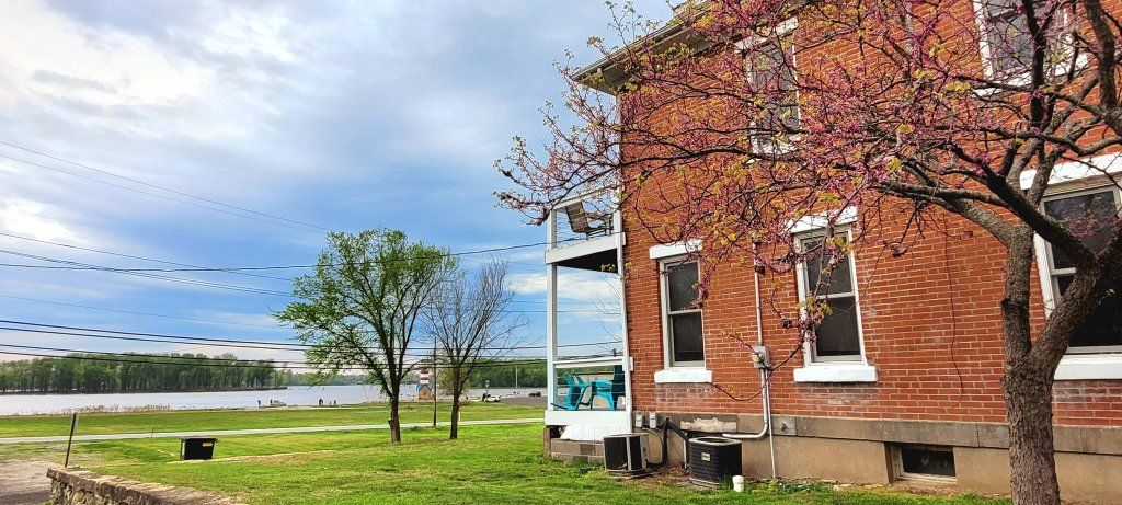 A brick building with a tree in front of it and a lake in the background.
