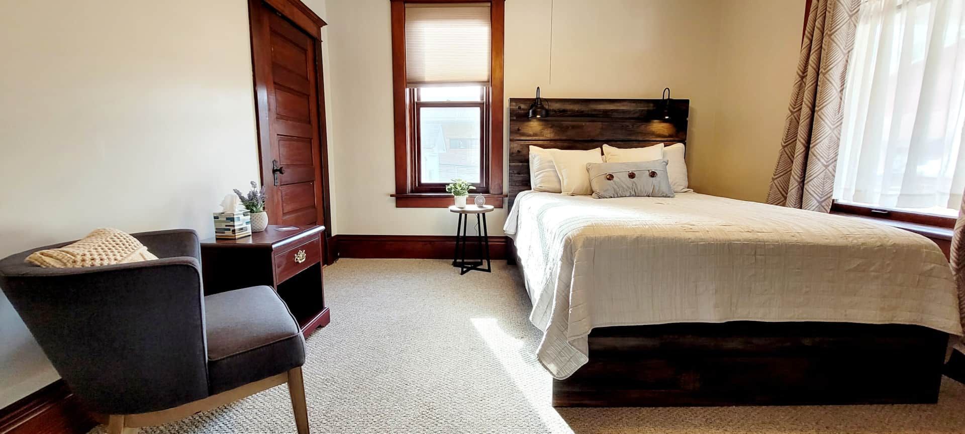 A bedroom with a bed , chair , nightstand and window.