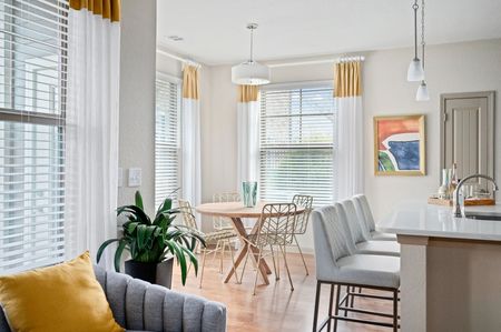 A dining area with a round wood table, metal chairs, hanging pendant lights, and large windows with white and gold drapes.
