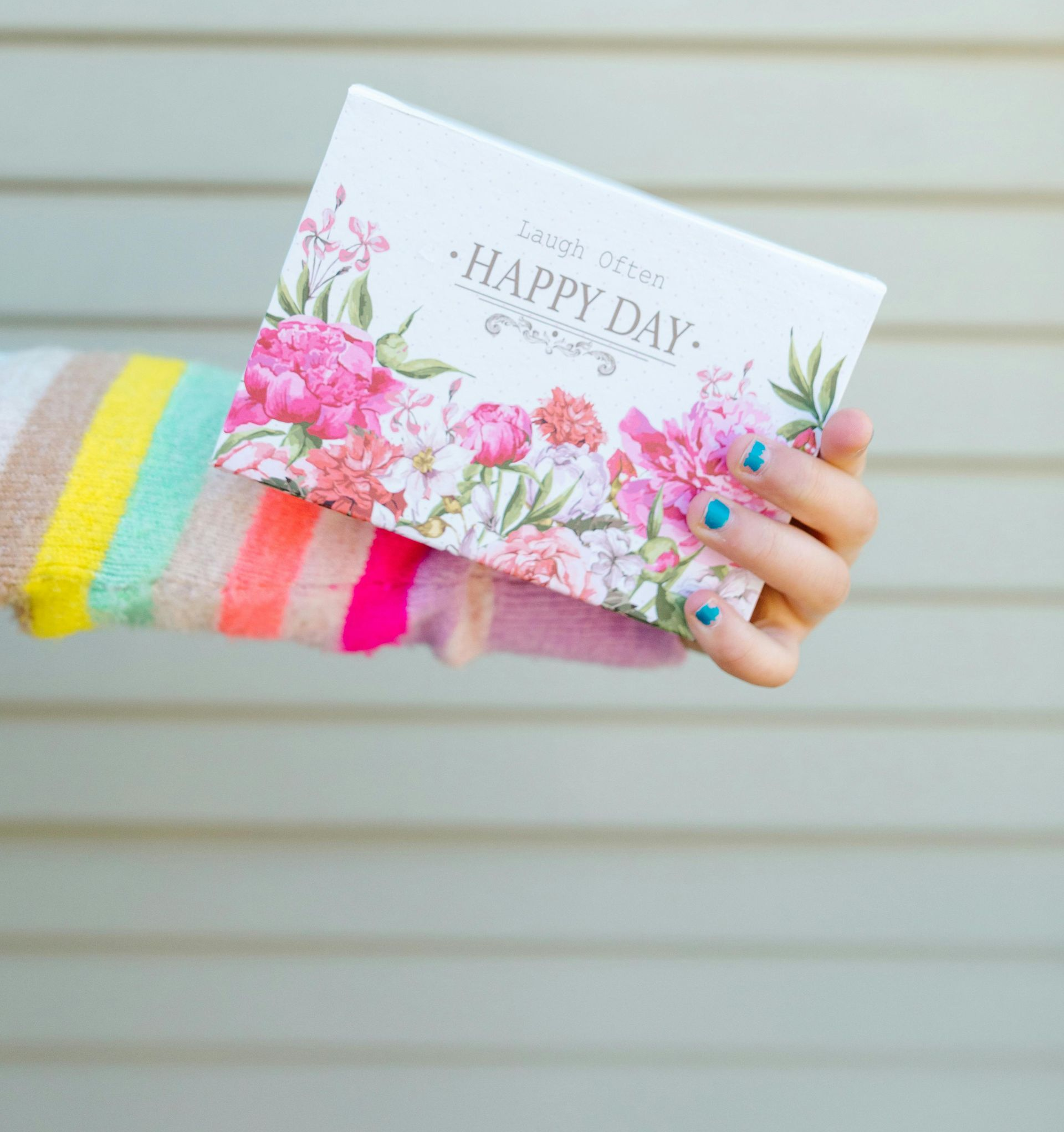 Person holding a floral card that says “Happy Day” with a colorful striped sleeve.