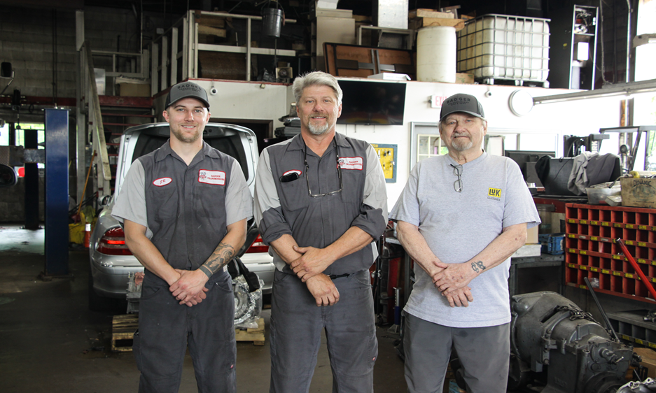 Three men are posing for a picture in a garage Three men are posing for a picture in a garage