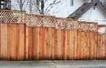 A wooden fence is sitting on the side of the road next to a house.