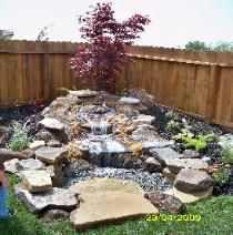 A waterfall in a backyard with a wooden fence in the background.