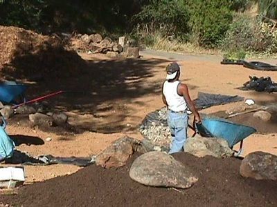 A man is standing in the dirt with a wheelbarrow
